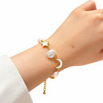 A delicate gold-tone bracelet with a star, pearl, and crescent moon charm, worn on a person's wrist in a warm, softly blurred indoor setting.