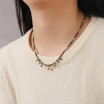 Necklace with multicolored beads and charms on a person wearing a beige sweater.
