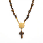 A necklace featuring brown tiger's eye beads, a gold-tone Saint Benedict medallion, and a matching wooden cross pendant, displayed on a clean white background.