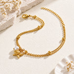 A delicate gold chain anklet featuring a starfish and pearl charm, displayed on a textured cream surface with soft shadows.