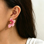 Close-up of a person wearing a pink floral earring with gold accents.