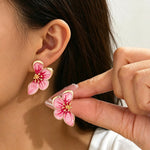 Close-up of a person wearing pink floral earrings with gold centers.