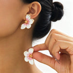 Flower-shaped earrings being worn and held by a person with a neutral background
