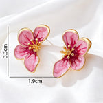 A pair of flower-shaped stud earrings with pink marbled enamel petals and gold-tone borders and center details, shown on a white satin-like background with measurement lines indicating 3.3 cm height and 1.