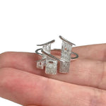 A silver open ring with three textured rectangular bar elements and curved metal accents, shown resting on a person's fingers against a white background.