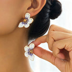 Flower-shaped earrings being worn by a person with a blurred background