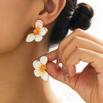 Flower-shaped earrings being worn with a blurred background